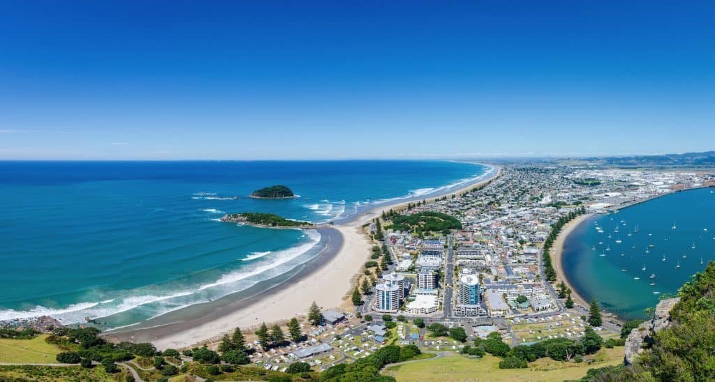 View from Mount Maunganui looking Southeast along the golden surf beach with Pilot Bay and Tauranga Harbour on the right and the Pacific Ocean stretching to the horizon.