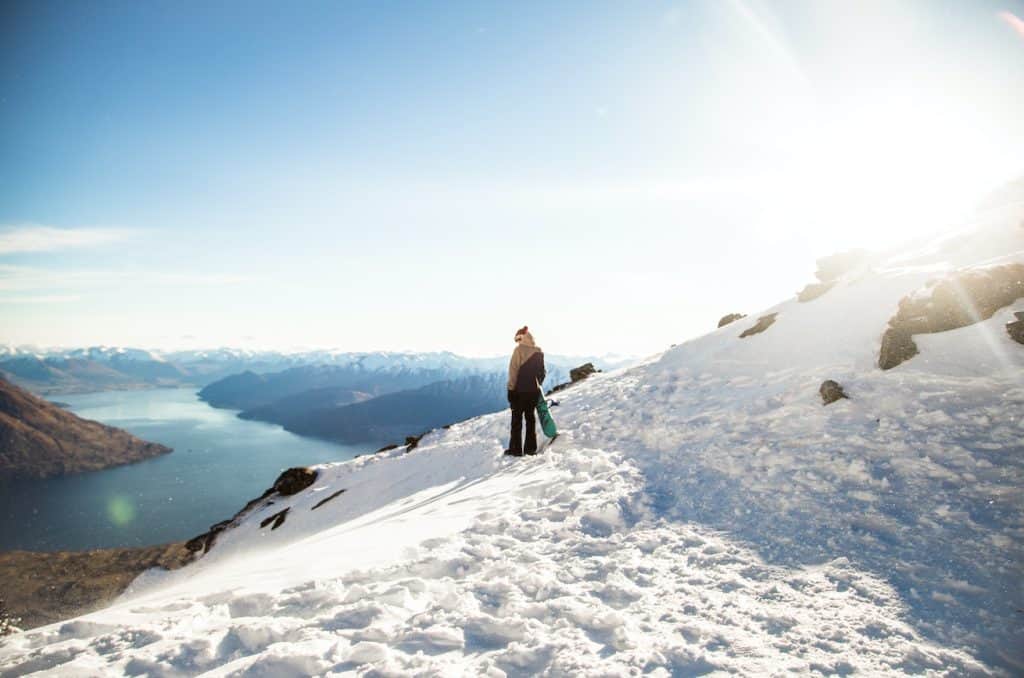 A snowboarder on the snowy ski trails at Cardrona Alpine Resort, against a backdrop of the Southern Alps mountain range.