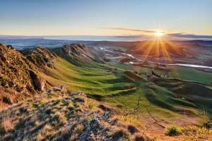 A beautiful sunrise over the ocean horizon in Hawke's Bay, casting vibrant orange and golden light across the calm water and pebble shoreline.