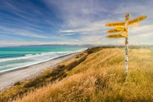 Scenic coastal view with signposts pointing to Southland and Fiordland in New Zealand.
