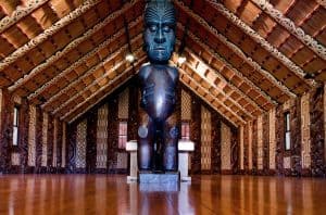 Traditional Maori meeting house with carved wooden figure in New Zealand.