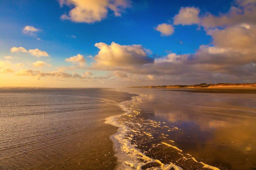 A dramatic golden sunset over the vast, empty sands and crashing ocean waves of Ninety Mile Beach (Te Oneroa-a-Tōhē) in the Far North of New Zealand.