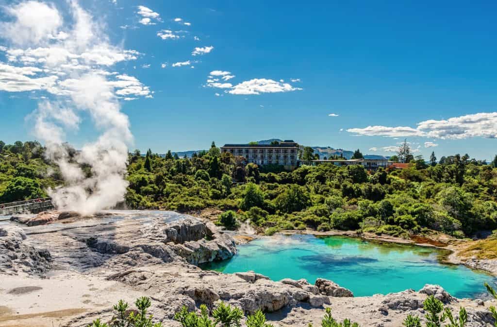 The active Pōhutu Geyser erupting with steam alongside a vibrant blue geothermal pool in the Te Puia Geothermal Valley, Rotorua.