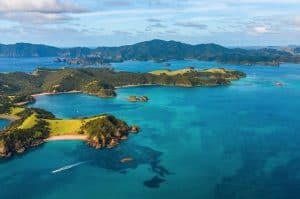 Here are a few great alt text options for your general Bay of Islands image, tailored to match the specific layout or feel of the shot: Option 1: Panoramic or Landscape Focus (Highly Recommended) Panoramic aerial view of the Bay of Islands, showcasing scattered green islands, sheltered coves, and pristine, crystal-clear blue waters under a sunny sky.