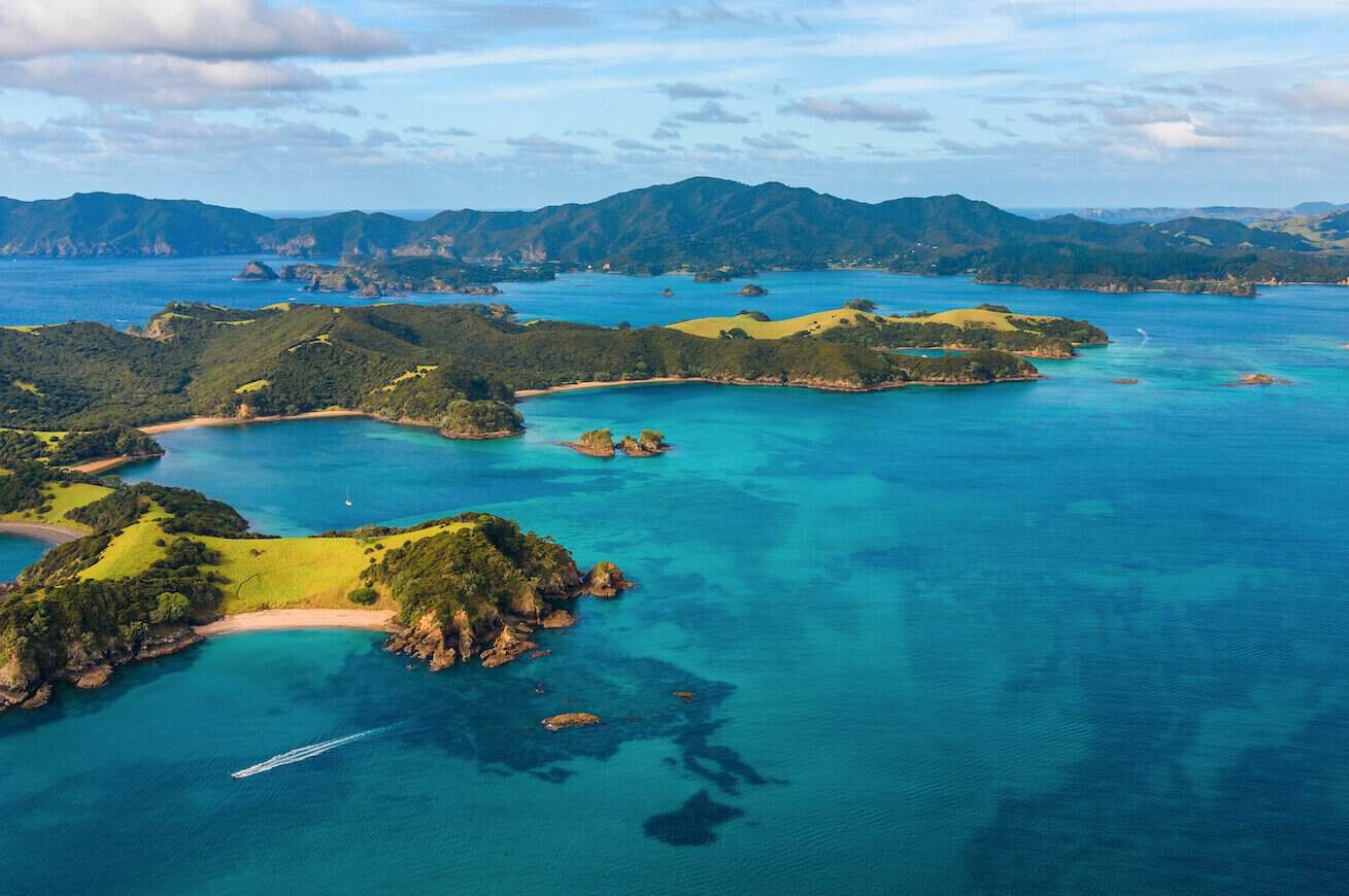 Here are a few great alt text options for your general Bay of Islands image, tailored to match the specific layout or feel of the shot: Option 1: Panoramic or Landscape Focus (Highly Recommended) Panoramic aerial view of the Bay of Islands, showcasing scattered green islands, sheltered coves, and pristine, crystal-clear blue waters under a sunny sky.